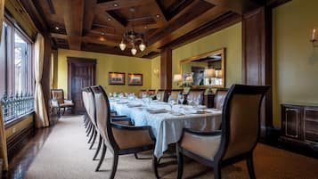 Uma sala de jantar formal com uma mesa comprida posta para refeição, vigas de madeira no teto e um lustre.