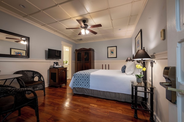 A bedroom with a bed, a ceiling fan, a television, a cabinet, and a small table with a lamp. - Hotel Grano de Oro (San José)