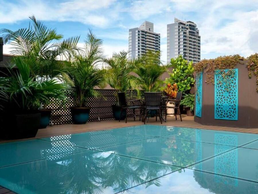 An outdoor pool area with a glass floor, surrounded by potted plants and a decorative fence.