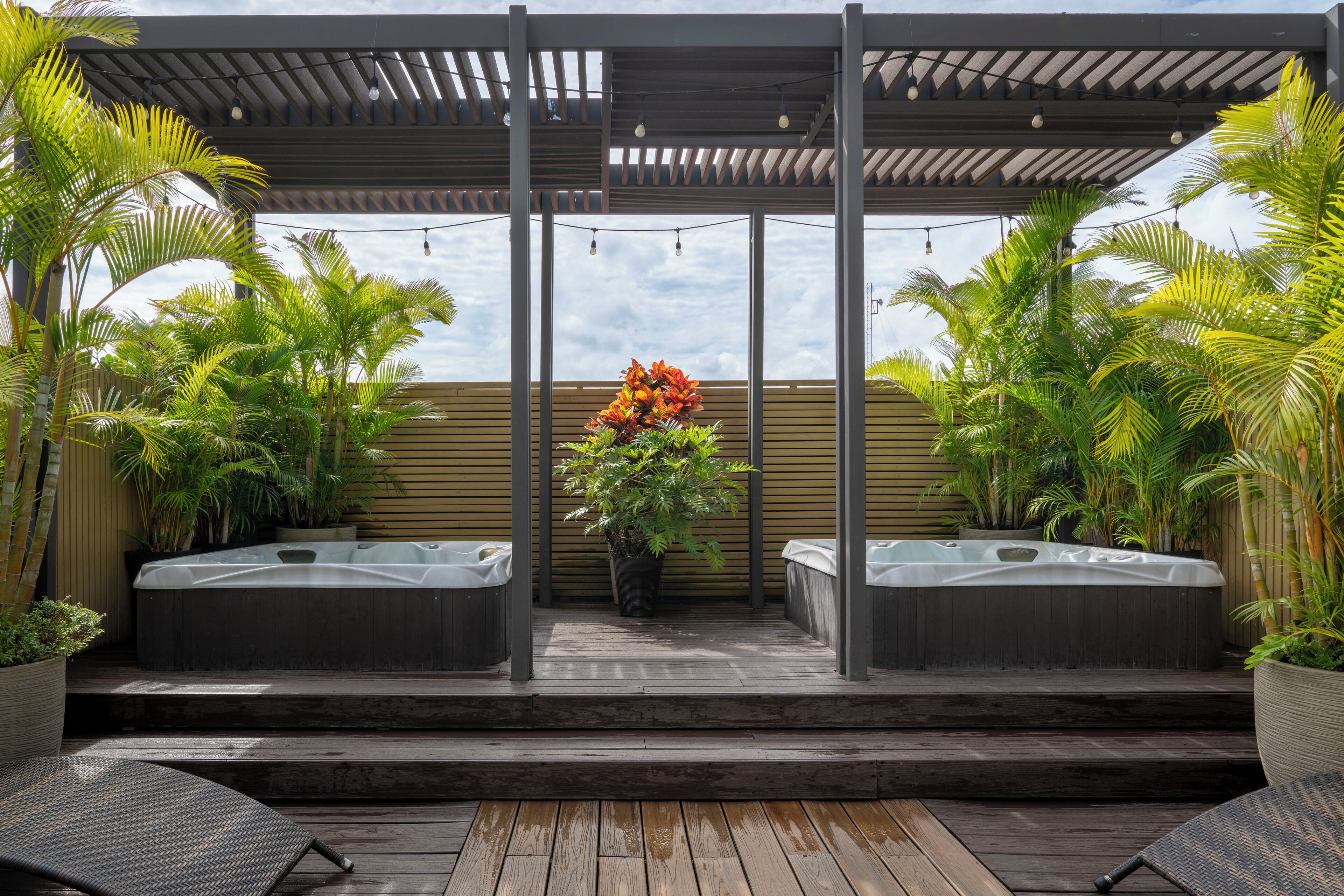 A covered outdoor area with wooden flooring, two hot tubs, and potted plants.
