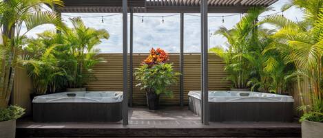 A covered outdoor area with wooden flooring, two hot tubs, and potted plants.