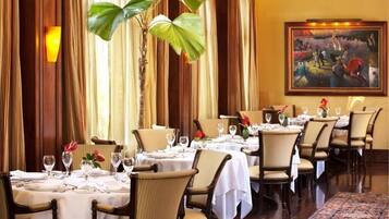 A dining area with tables set for a meal, chairs, and a large painting on the wall.