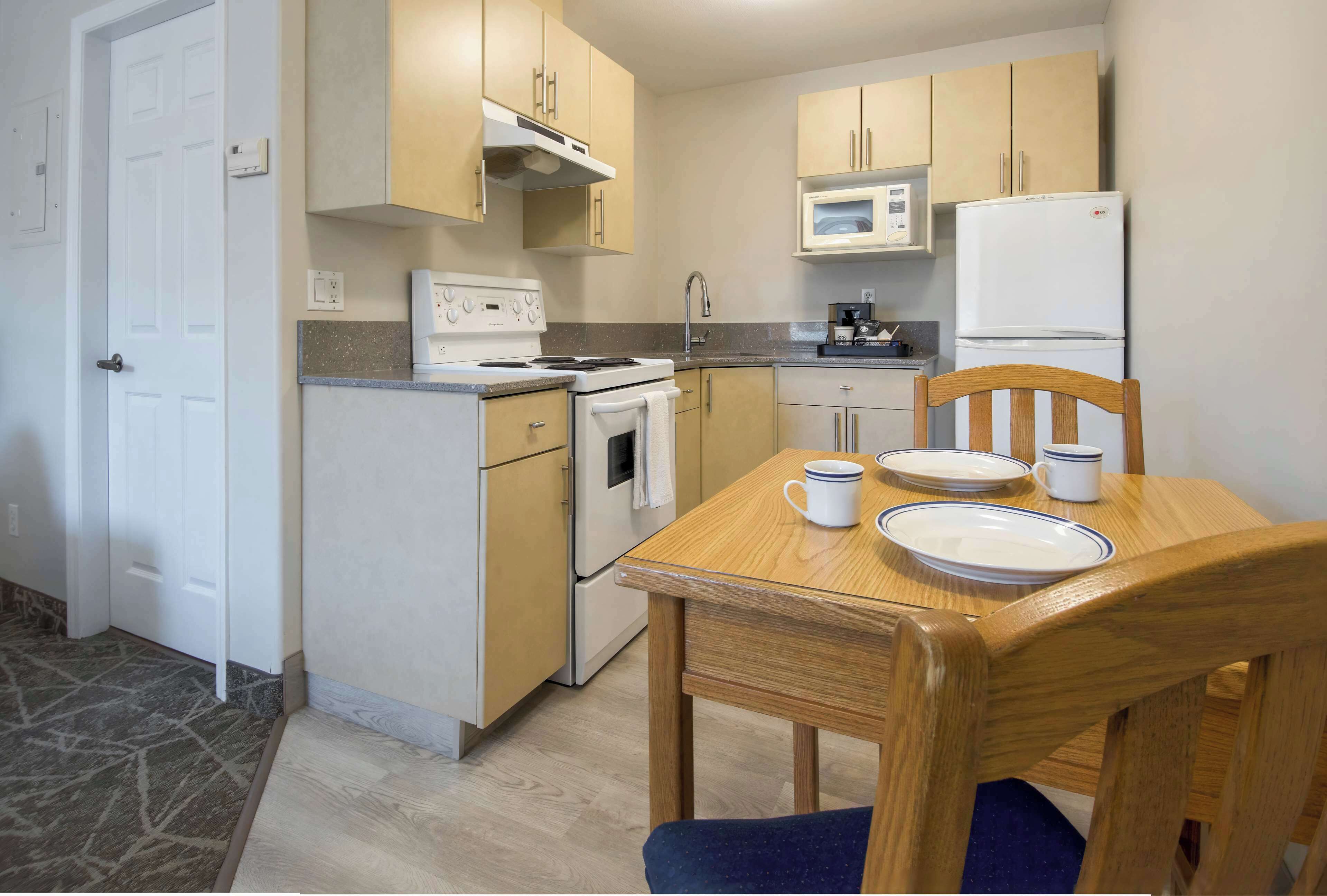 A compact kitchen with a stove, microwave, and refrigerator. There is a dining table with chairs and a small cabinet above it.