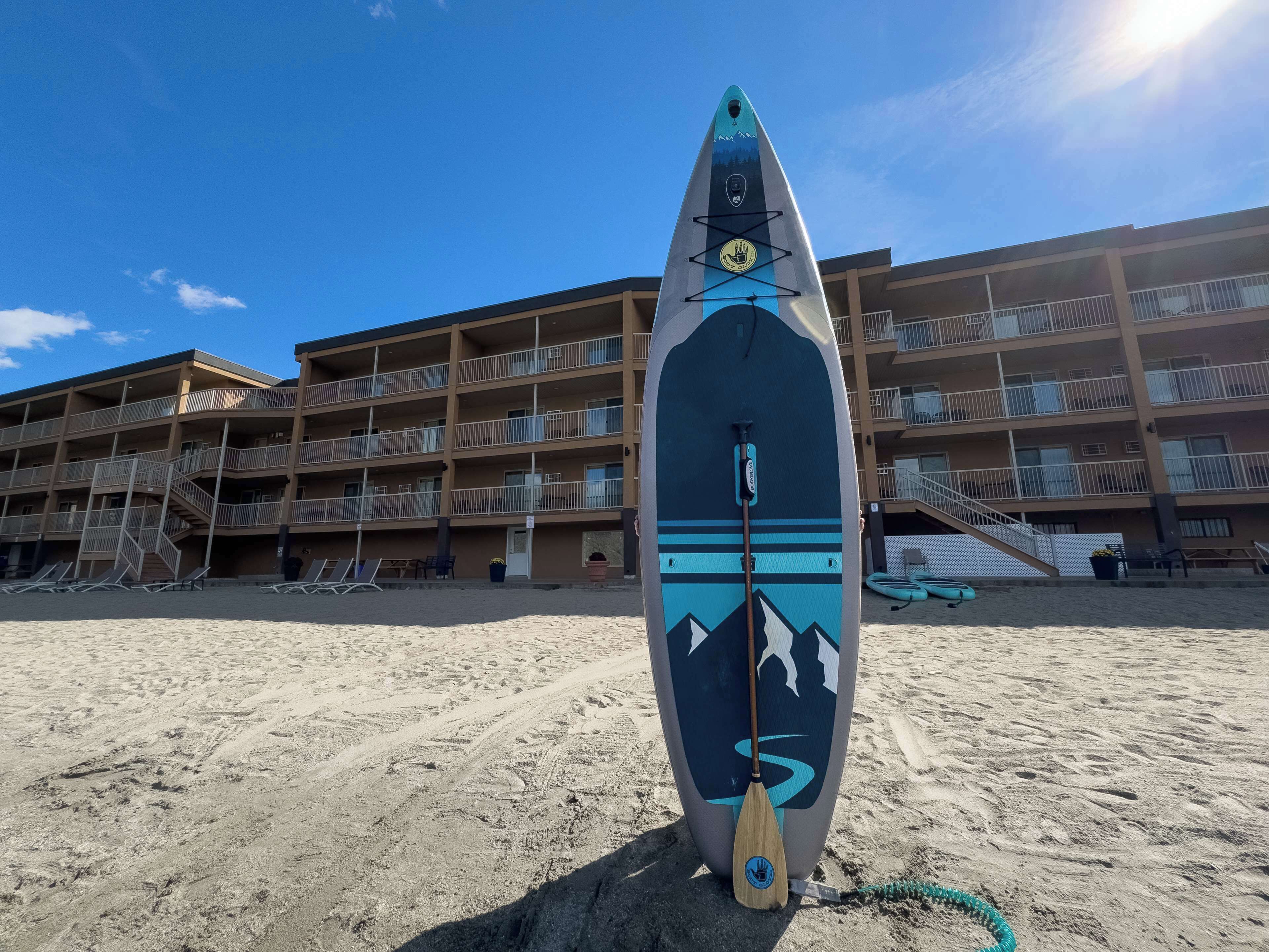 Une planche de surf sur une plage de sable, avec un immeuble à plusieurs étages en arrière-plan.