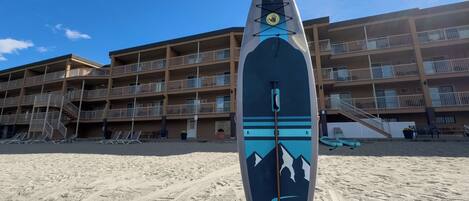 Une planche de surf sur une plage de sable, avec un immeuble à plusieurs étages en arrière-plan.