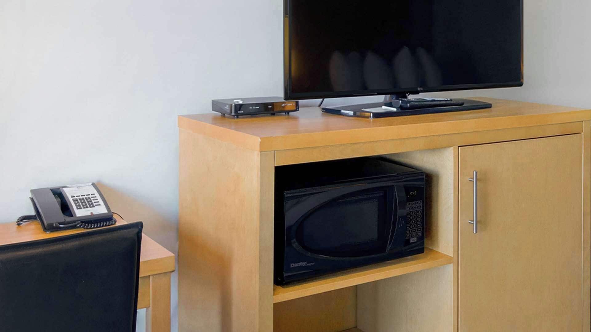 Een hotelkamer met een houten bureau, een flatscreen televisie, een magnetron en een telefoon.