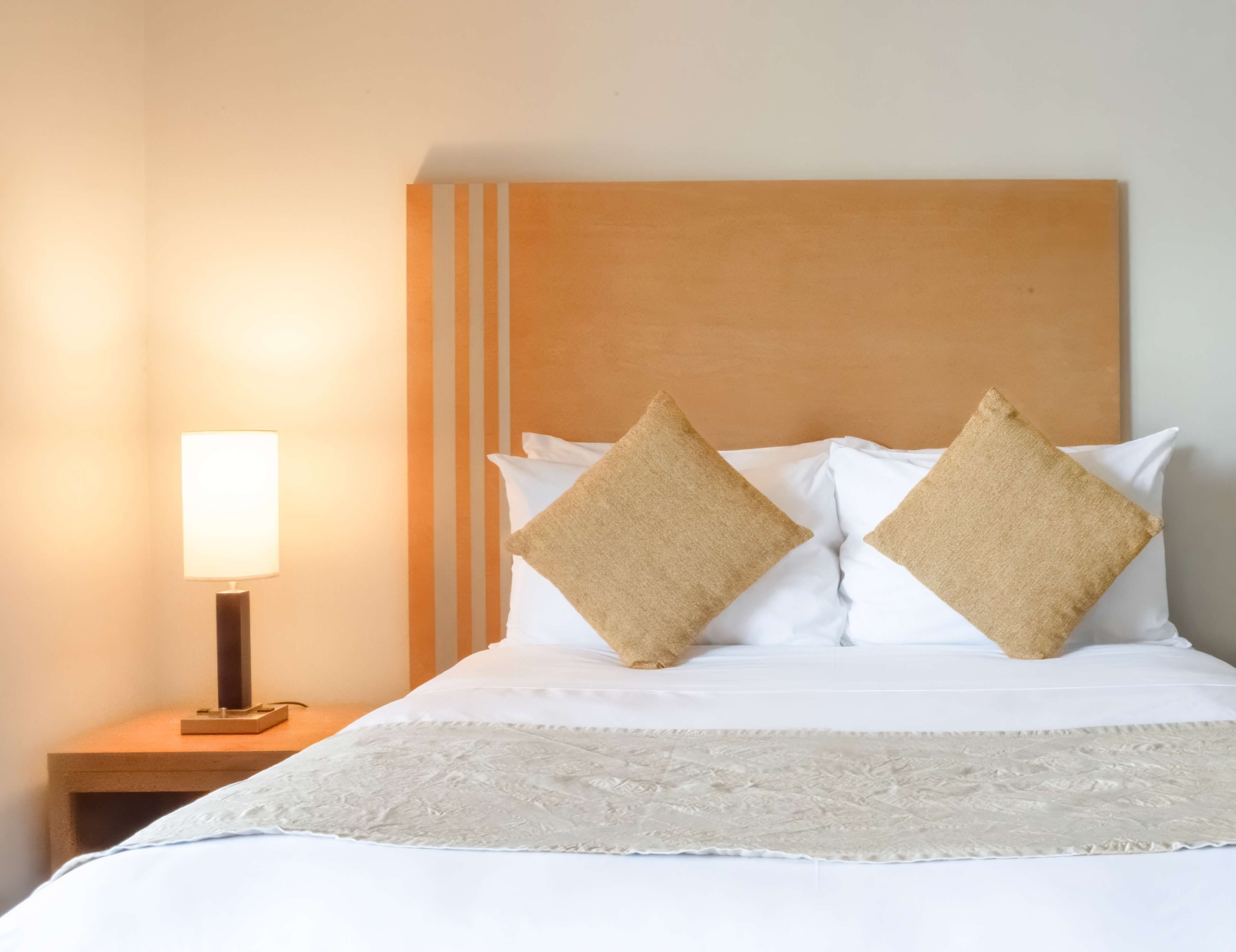 Una cama bien hecha con dos almohadas, una lámpara de noche y un edredón con textura.