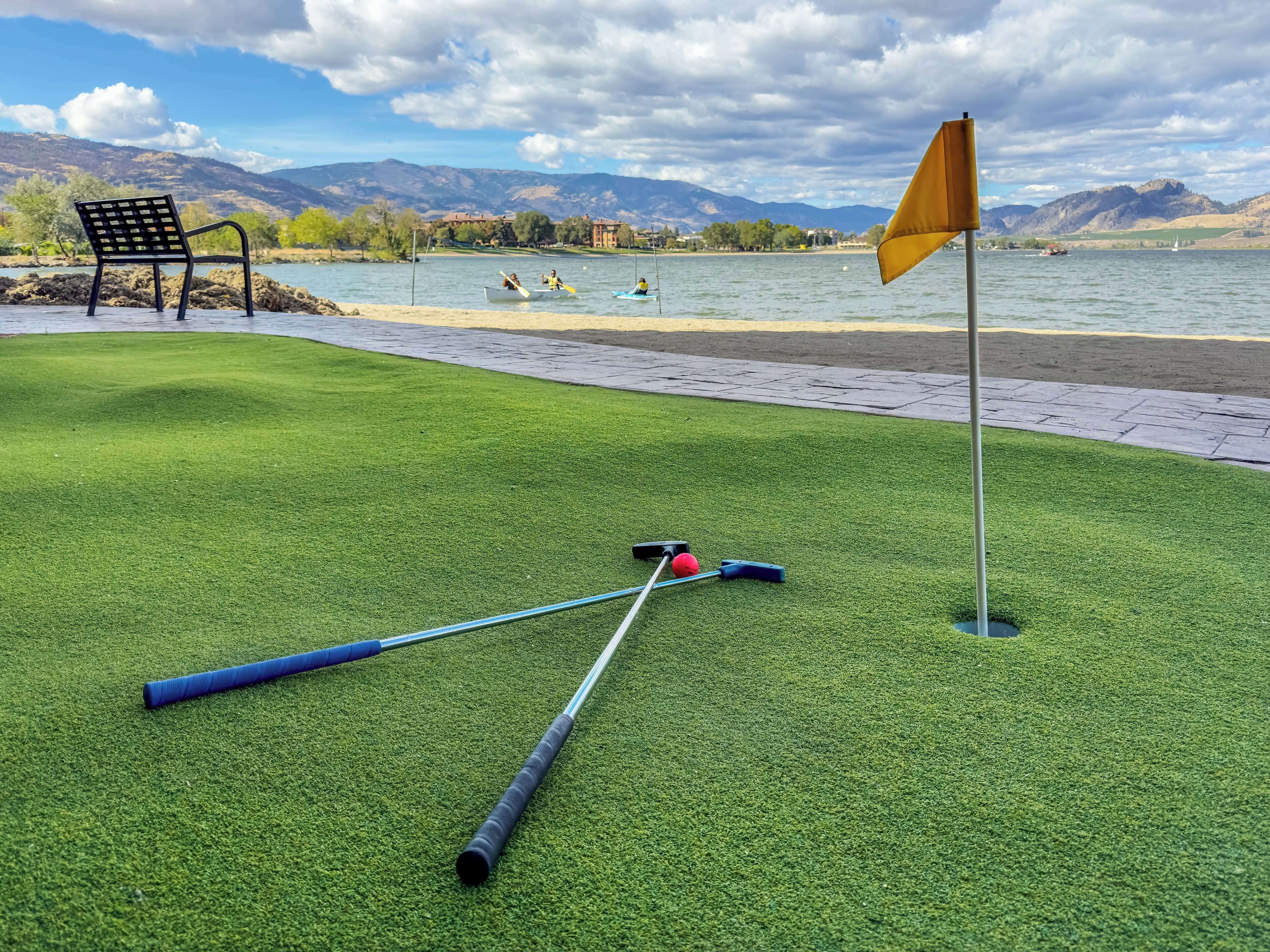 A golf course with a flag, a bench, and a water body in the background.