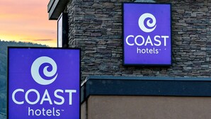 Two signs for COAST hotels, one larger and one smaller, mounted on a stone building with a tiled roof. - Coast Osoyoos Beach Hotel (Osoyoos)