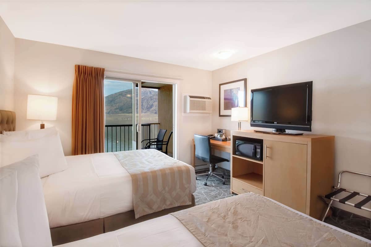 Habitación de hotel con dos camas, un escritorio, una televisión y vistas al exterior.