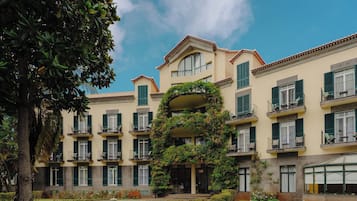 Un hotel de varios pisos con balcones, un césped cuidado y un jardín con diversas plantas y flores.