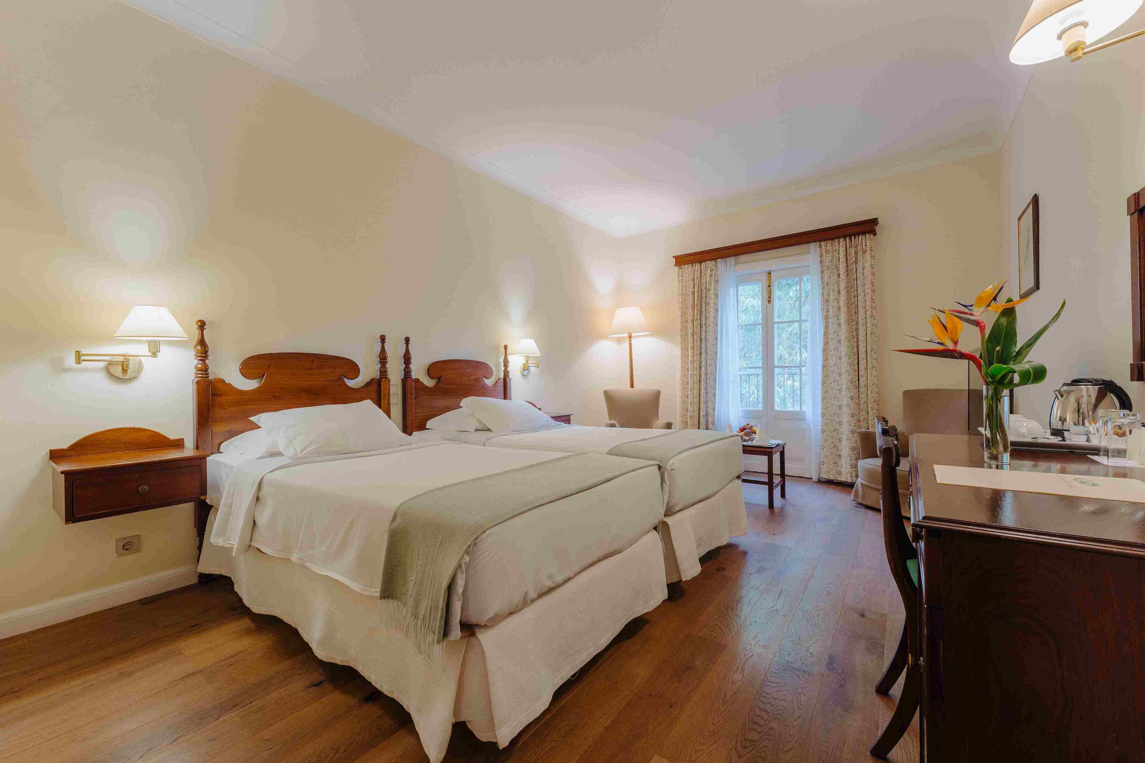 Quarto de hotel com duas camas, uma escrivaninha, uma cadeira e uma janela com cortinas.