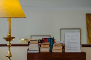 A stack of books on a wooden nightstand with a lamp and a menu card.