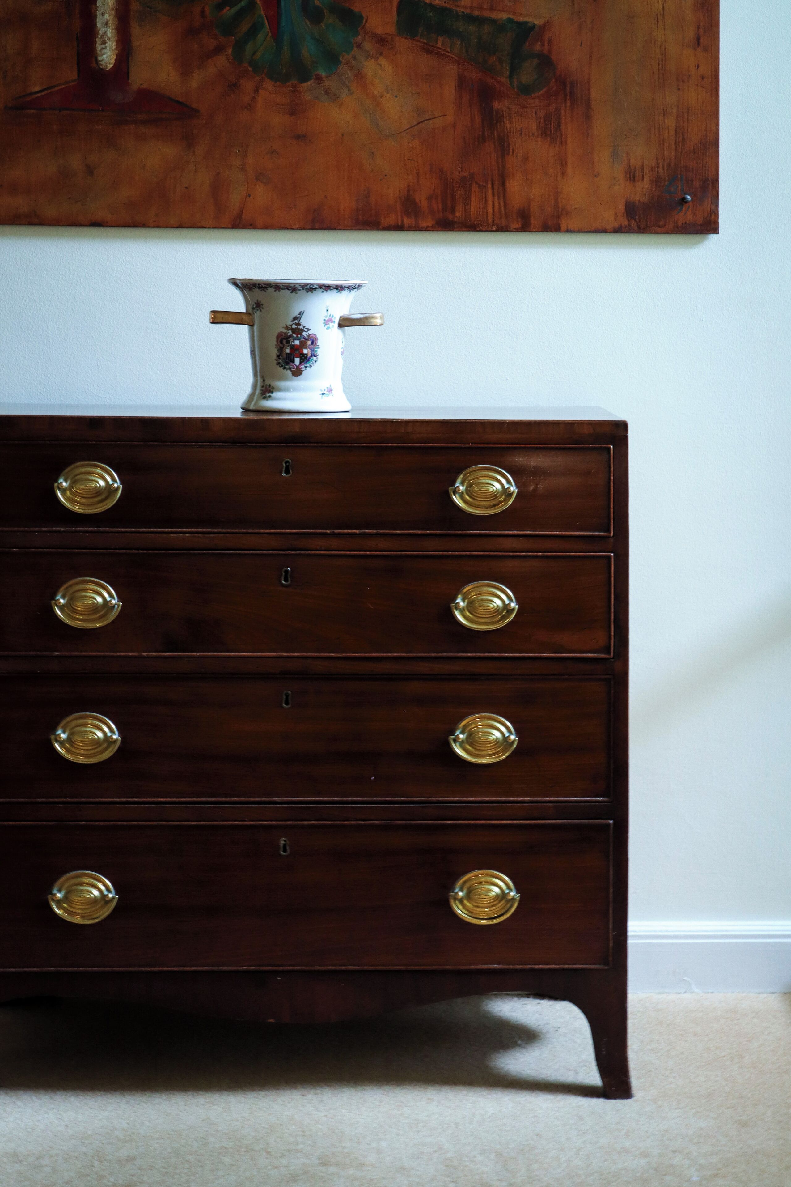 Un aparador de madera con tiradores de latón y un jarrón decorativo encima.