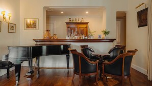 A grand piano, a dining table with chairs, a bar area, and a framed picture on the wall.