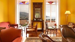 A living room with a red sofa, wooden chairs, a table, and a view through a window.