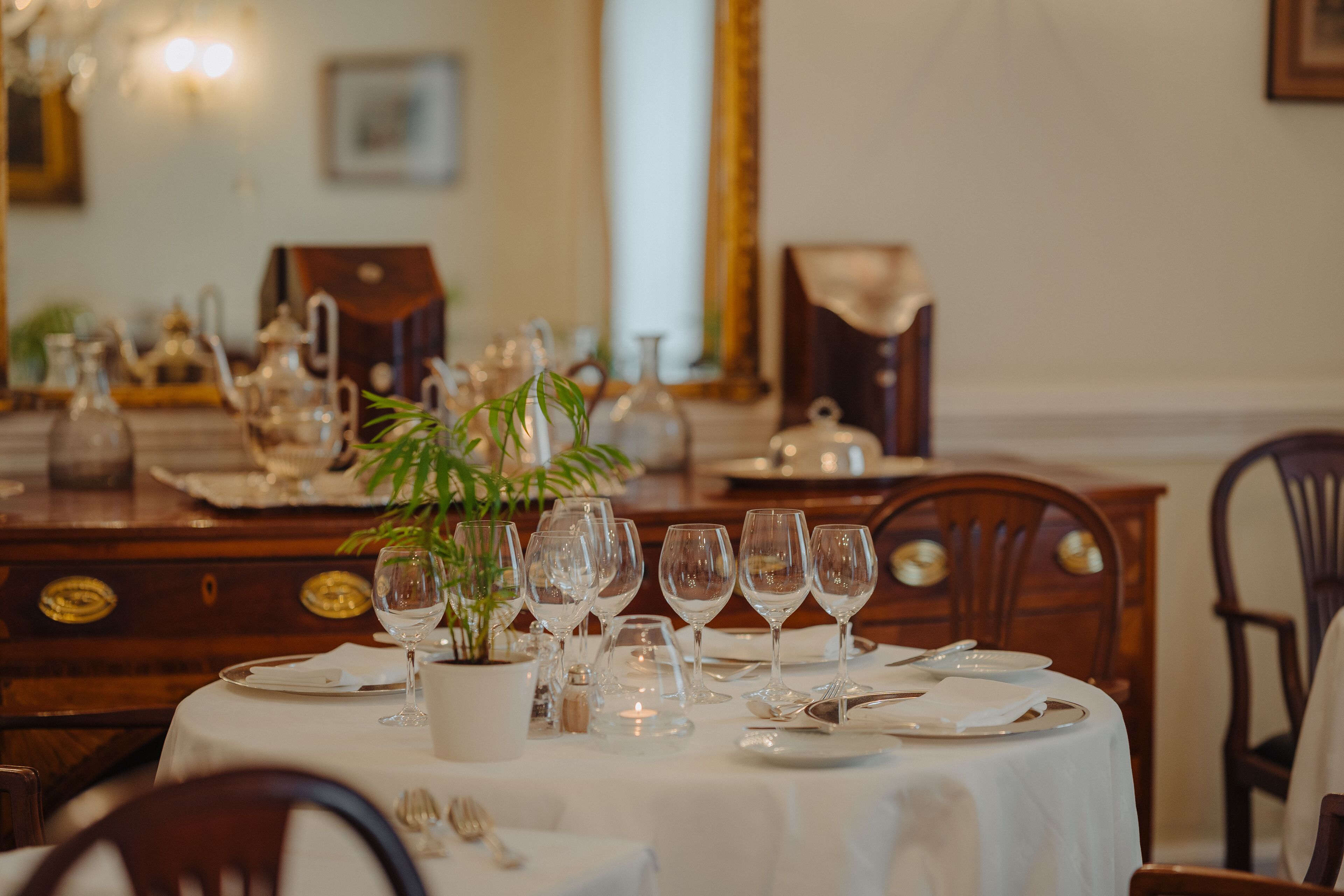 A dining table set with white tablecloth, clear glassware, and a potted plant.