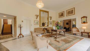A spacious living room with a large chandelier, a grand mirror, and a classic fireplace.