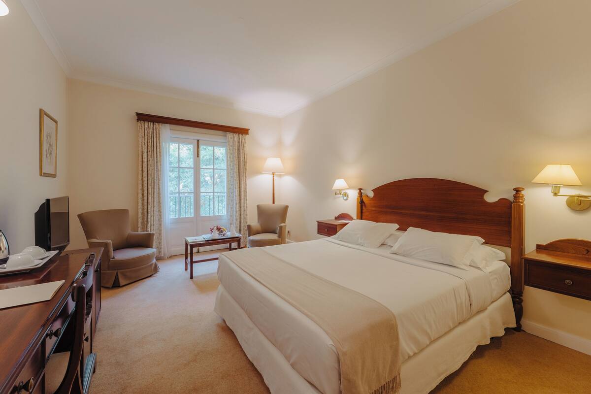 Habitació d'hotel amb un llit gran, un escriptori amb un ordinador, una cadira i dues làmpades de nit.