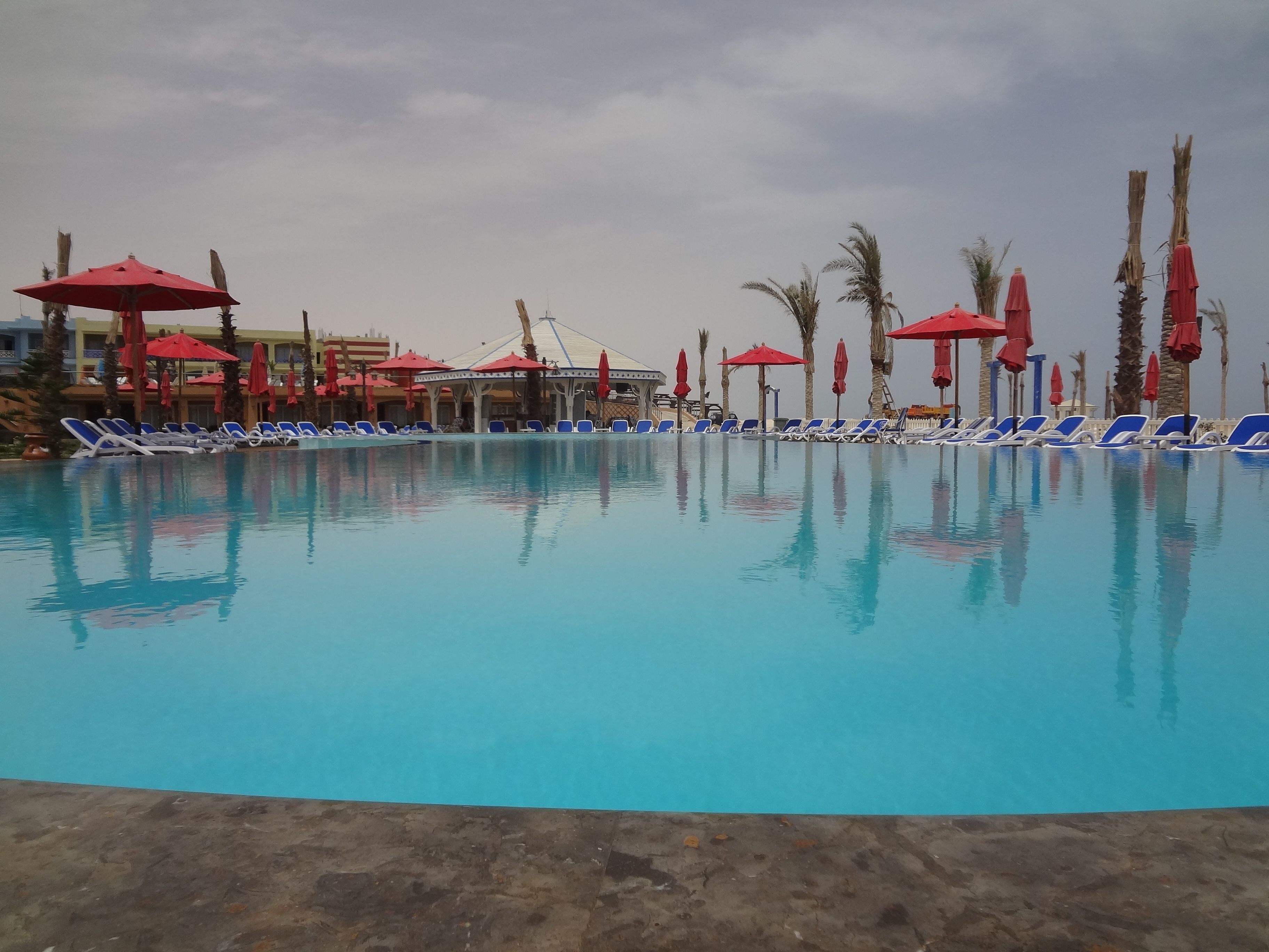 Une piscine à l’eau bleue, entourée de chaises longues et de parasols rouges.