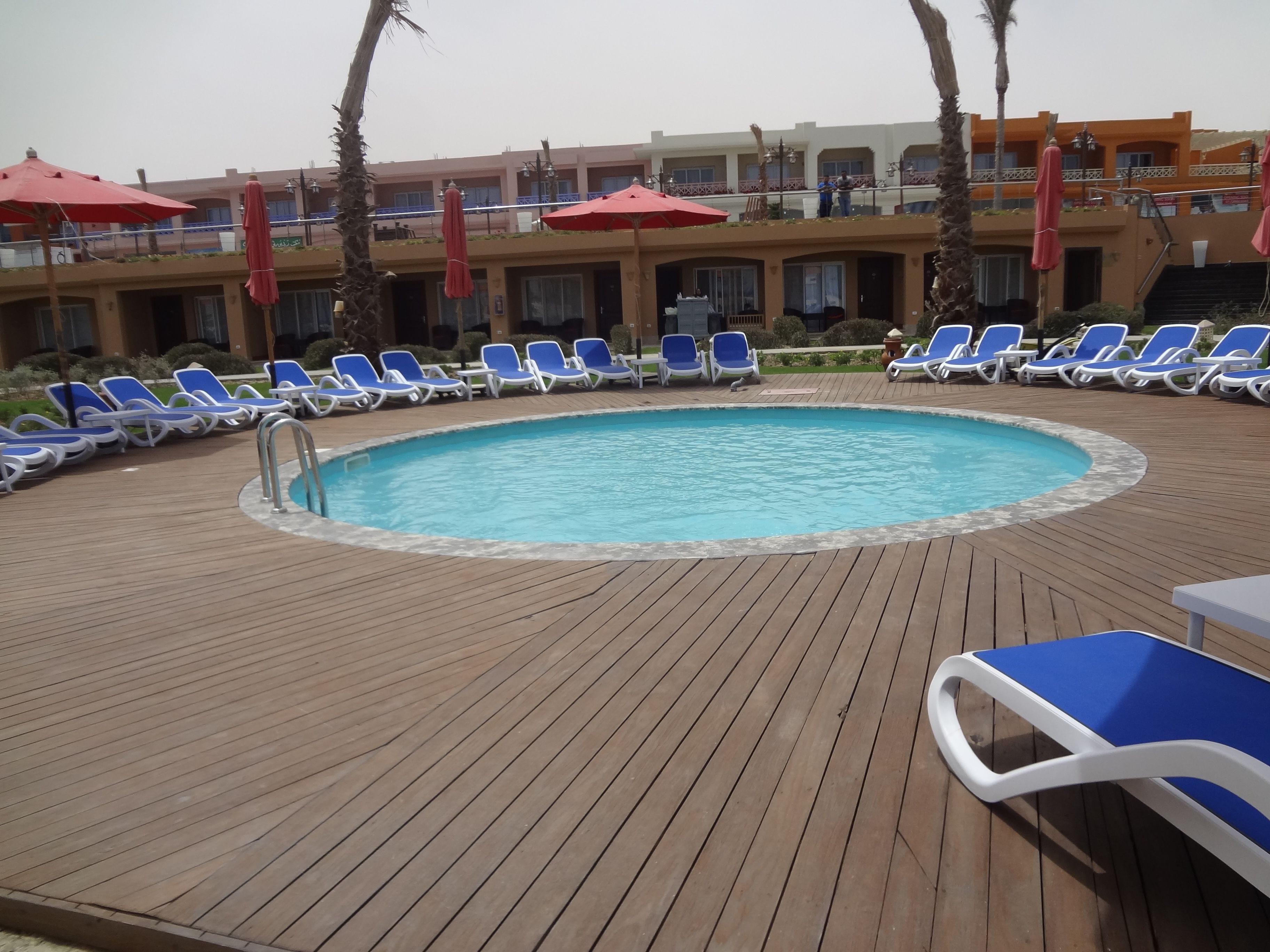 Un área de piscina con sillas reclinables azules y sombrillas rojas.
