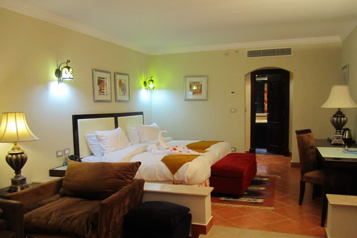 A hotel room with a bed, two chairs, a desk, and a lamp.