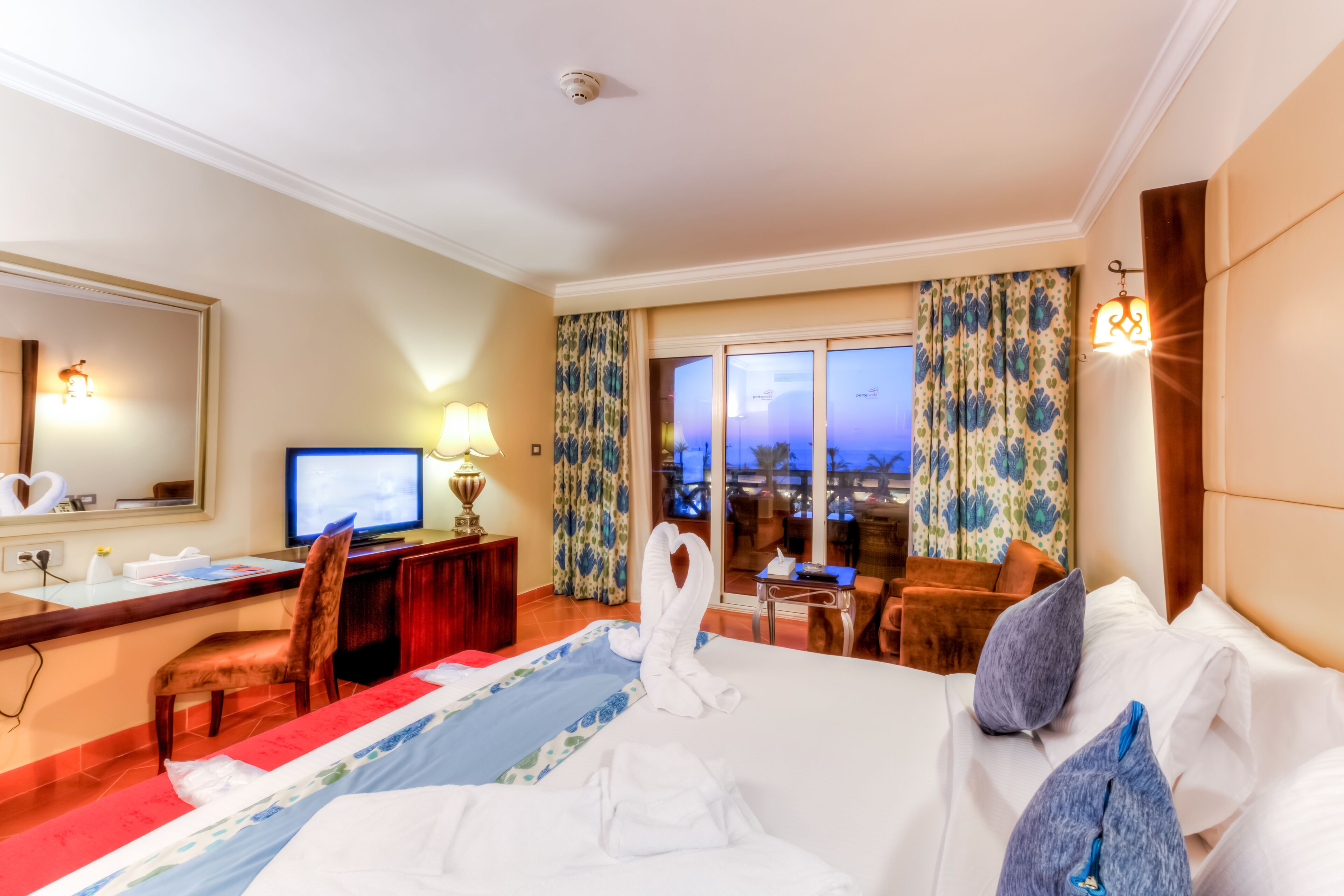 A hotel room with a bed, a desk, a chair, a television, and a view of the outside.