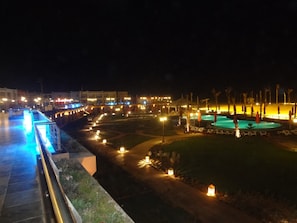 A nighttime view of a resort with a pool, illuminated pathways, and a bridge.