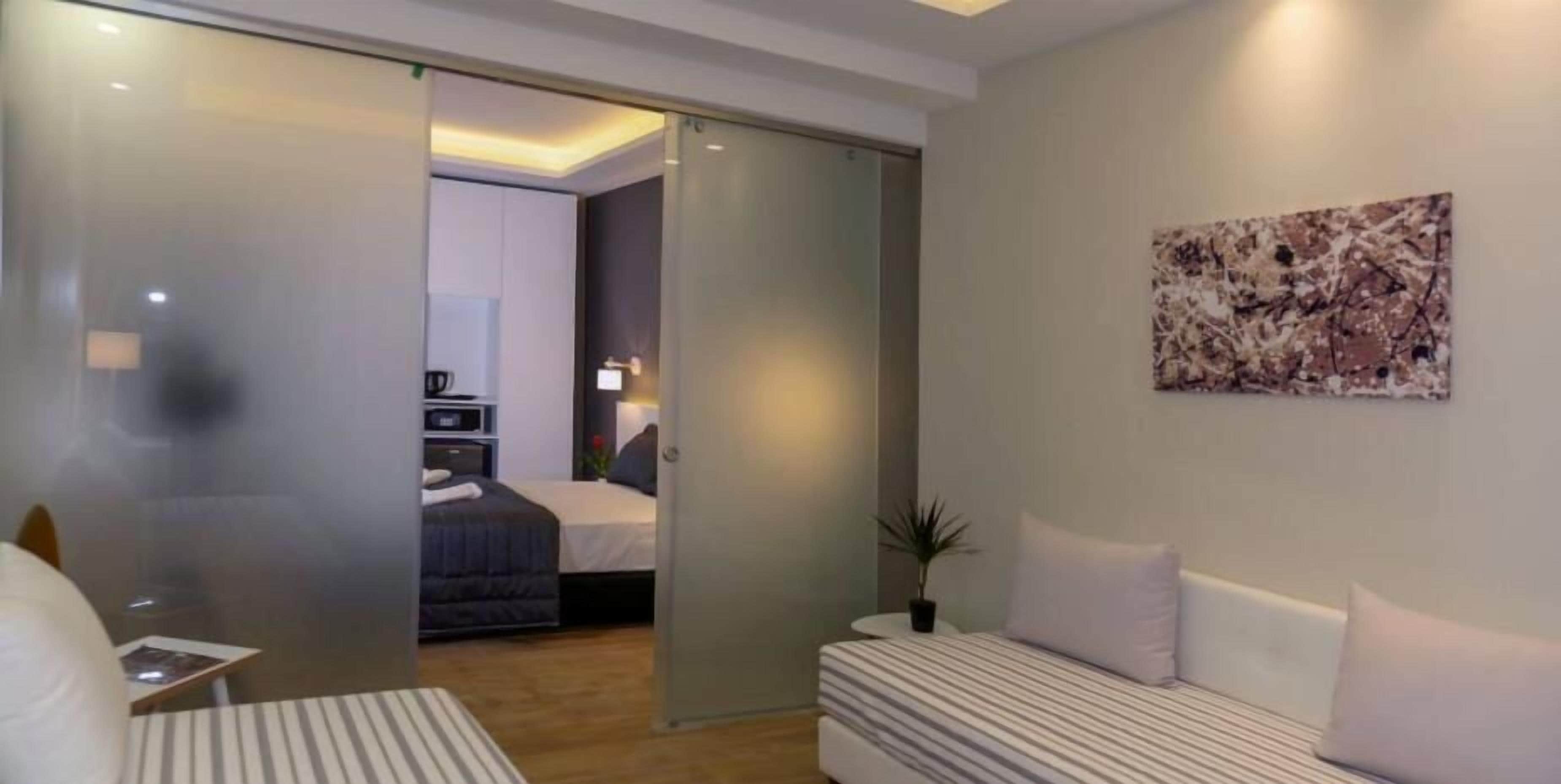 A modern hotel room with a bed, a bedside table, a small desk, a chair, a potted plant, and a painting on the wall.