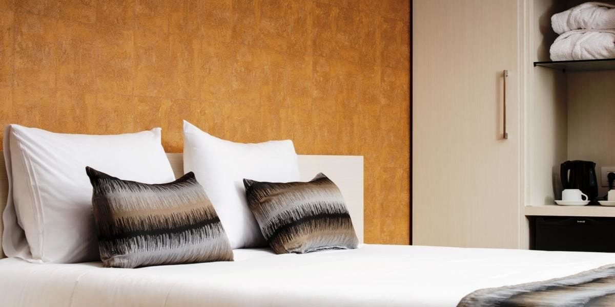 A hotel room with a bed, two pillows, a nightstand, and a coffee maker.