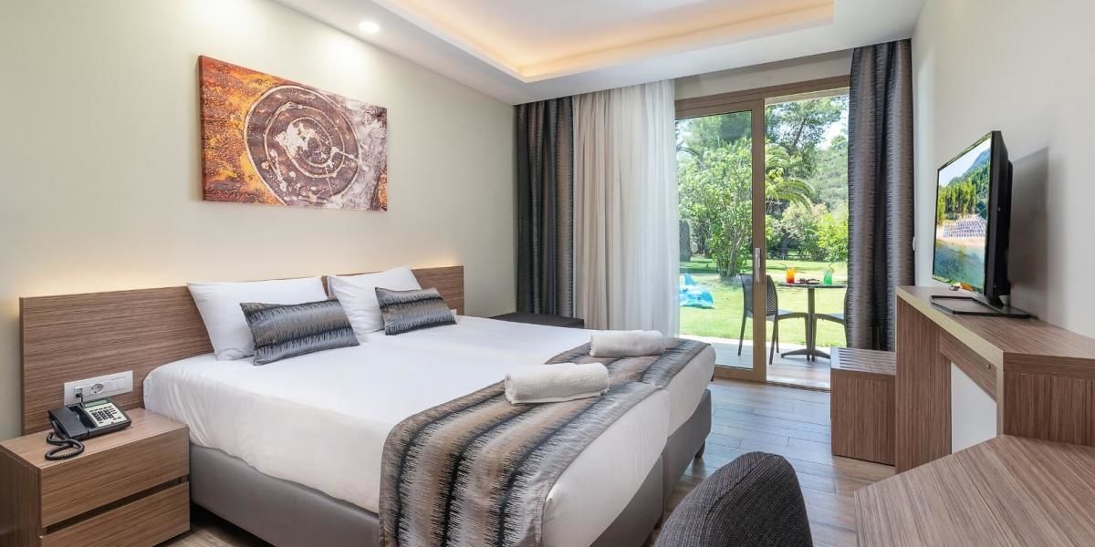 Habitación de hotel con una cama grande, un escritorio con televisor, teléfono y vistas al exterior.