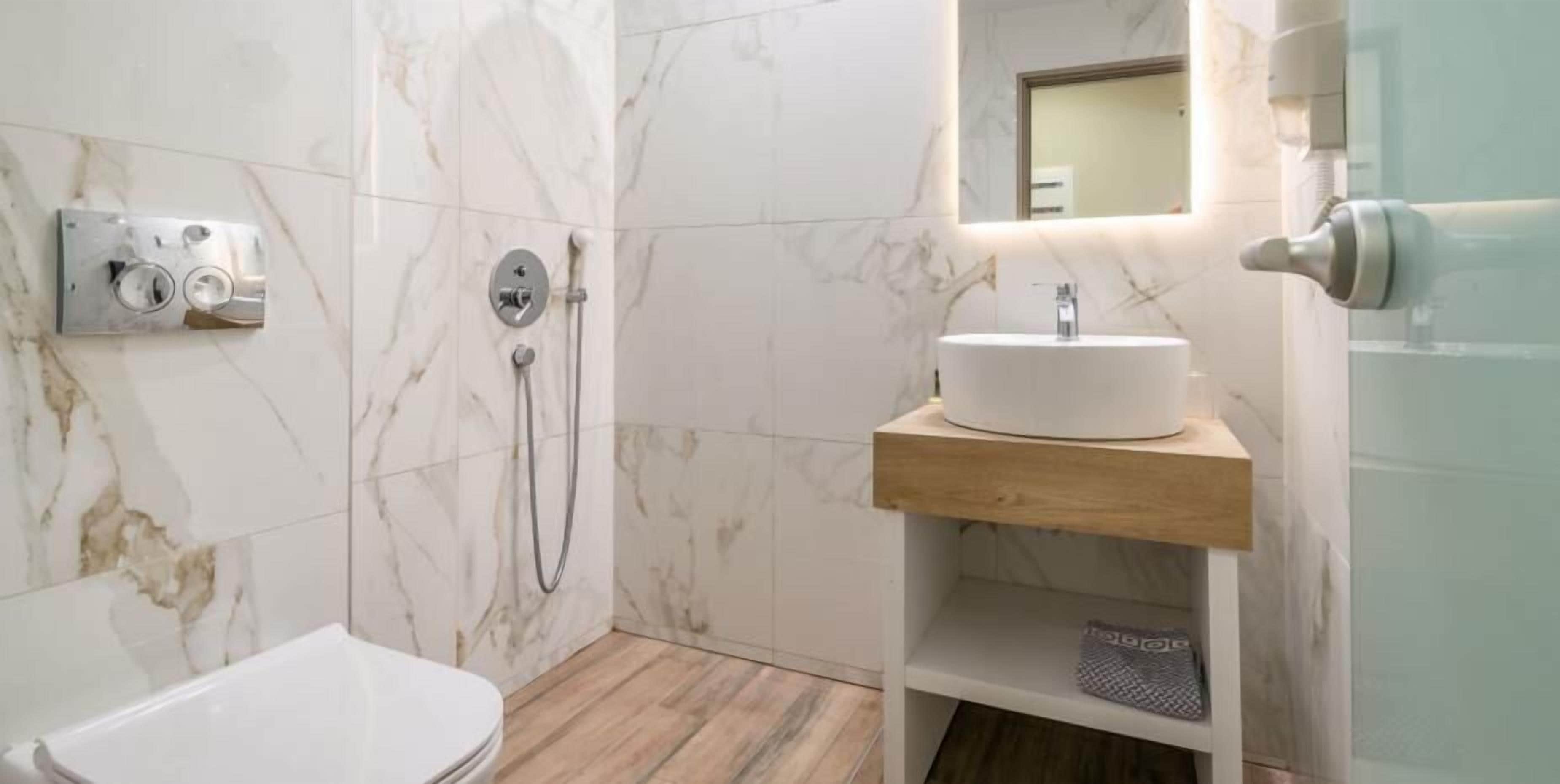 A modern bathroom with a marble wall, a wooden vanity, a white sink, and a shower with a handheld showerhead.