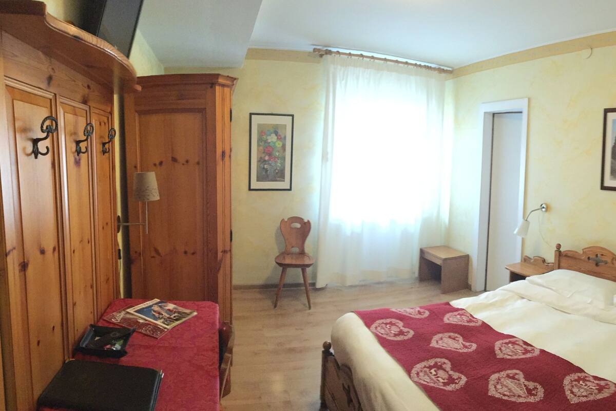 Un dormitorio con un armario de madera, una cama con colcha roja y blanca, una silla y un cuadro en la pared.