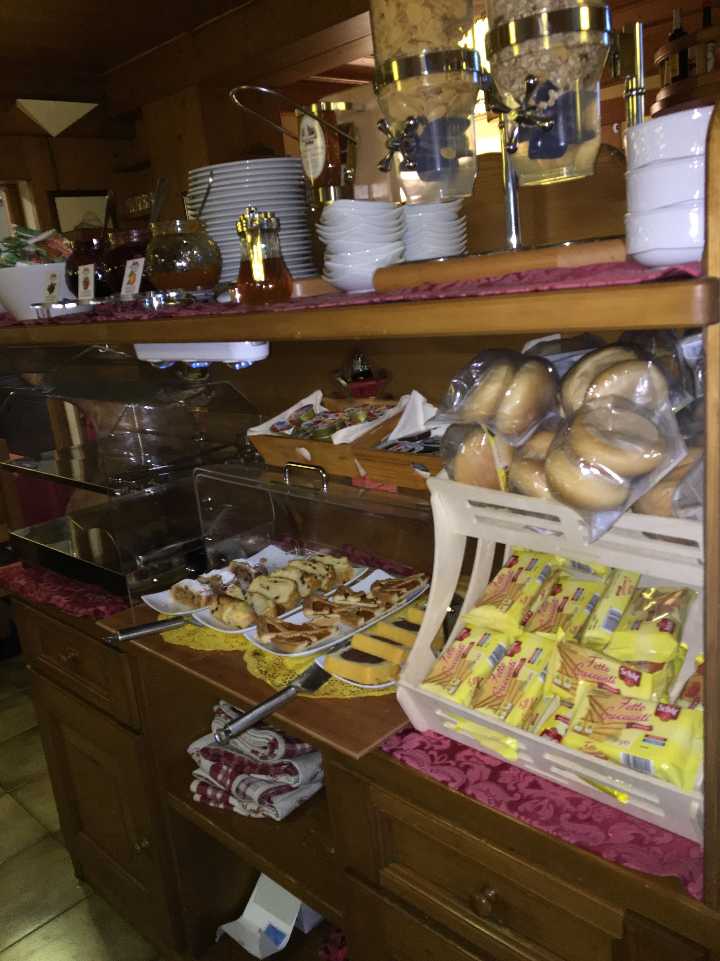 Zona de bufé con distintos alimentos, incluyendo pasteles y pan, expuestos en estantes y recipientes.
