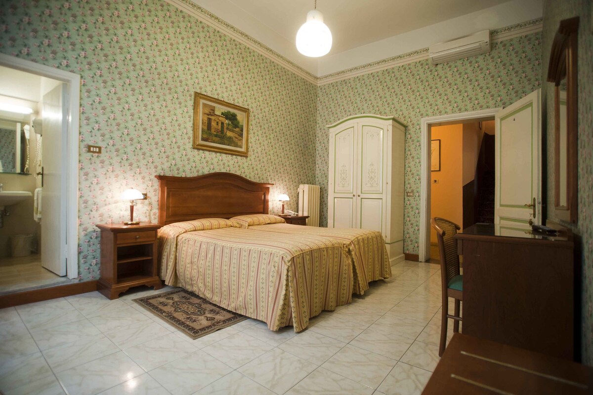 A bedroom with a bed, bedside tables, a dresser, a chair, and a door leading to another room.