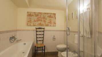 A bathroom with a bathtub, toilet, and bidet, a chair, and a shower area.