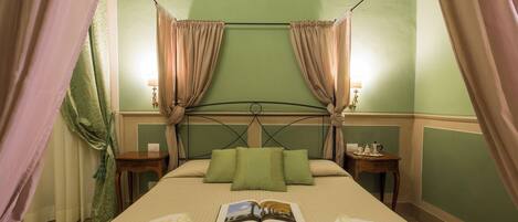 A neatly made bed with green pillows, a book, and folded towels. There are two bedside tables with lamps.