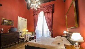 A hotel room with a bed, a desk, a chair, a television, a lamp, and a chandelier. - B&B La Bohème (Lucca)