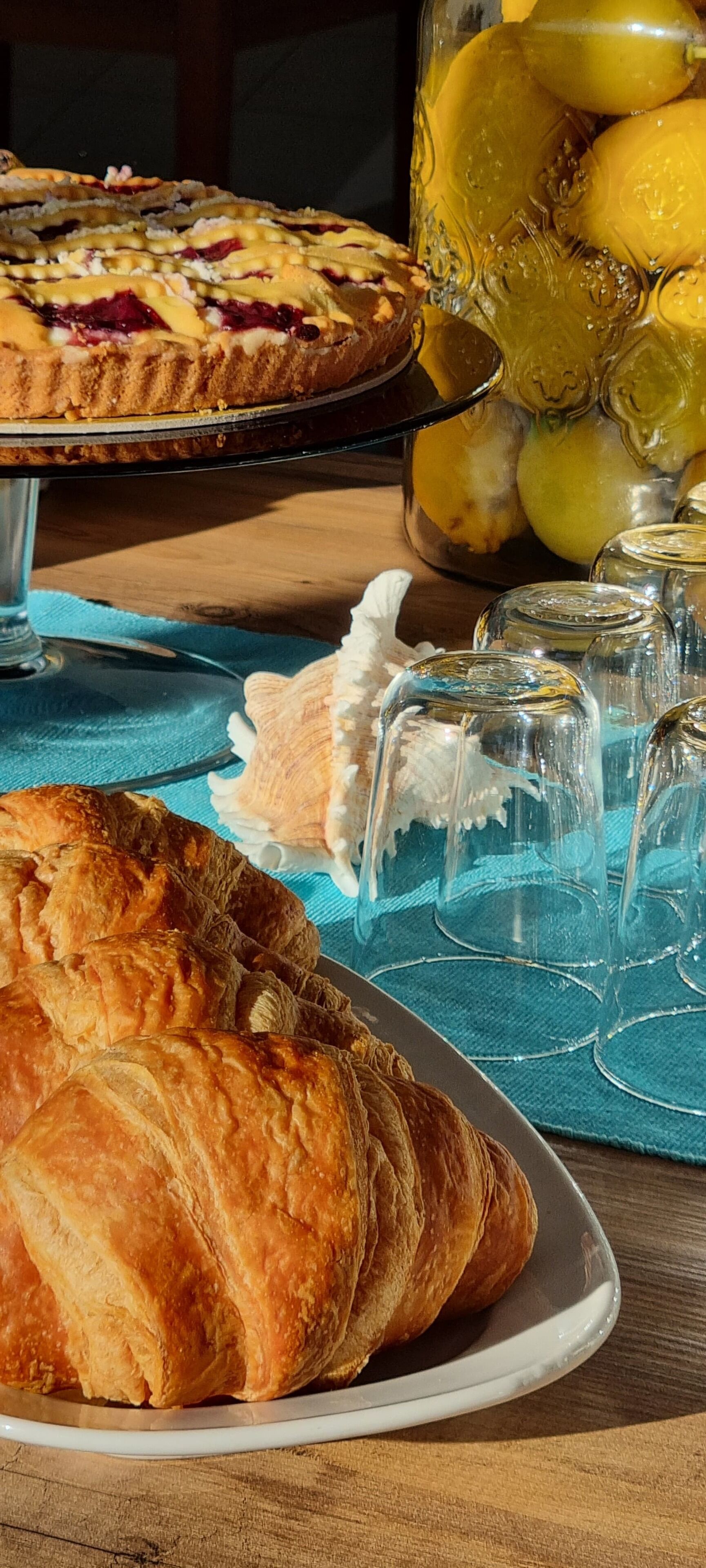 A table with a plate of croissants, a pie, and a glass jar with lemons.
