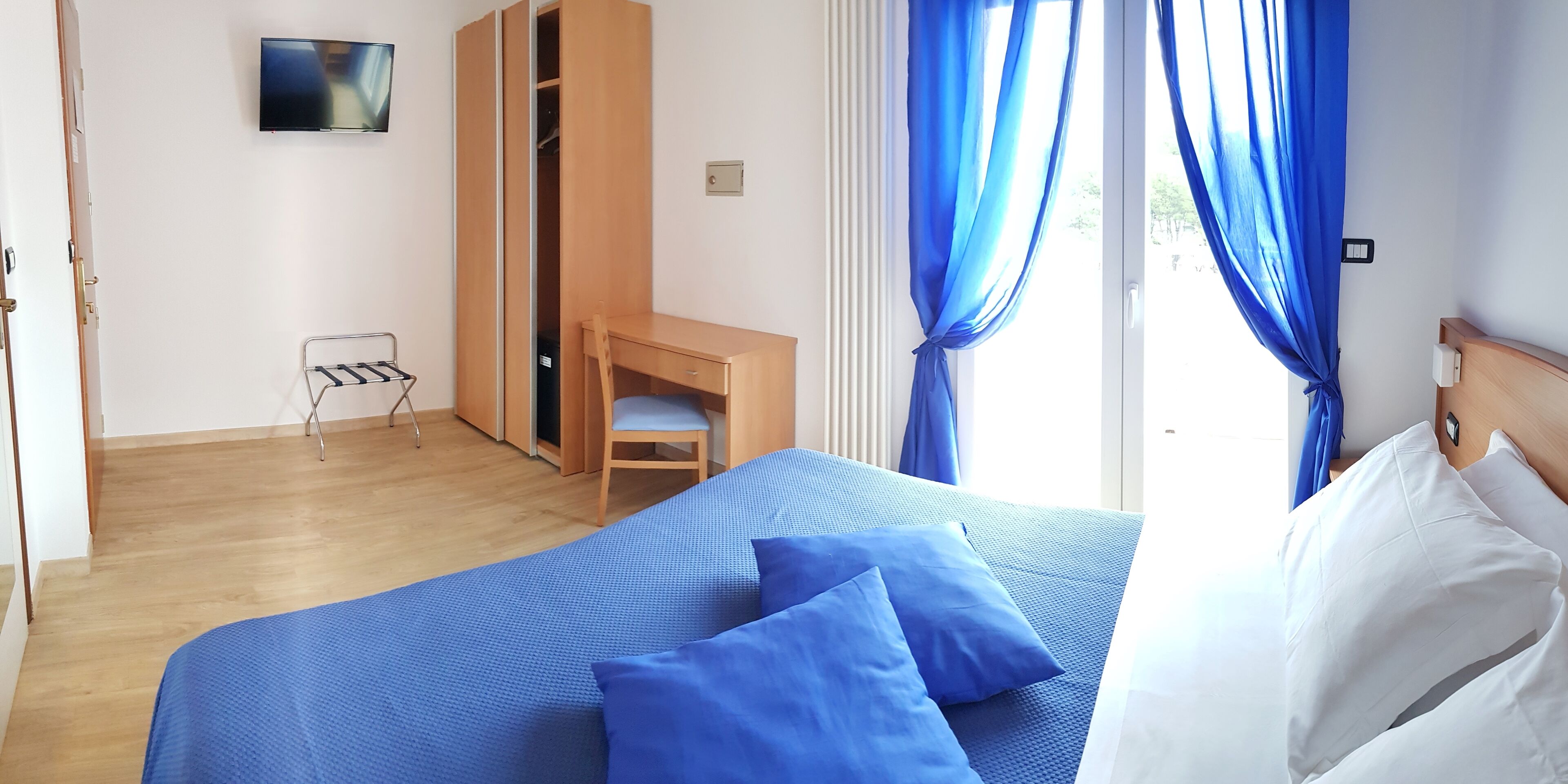Una habitación de hotel con cama, escritorio, silla y armario.