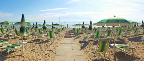 A beach with rows of sun loungers and umbrellas.