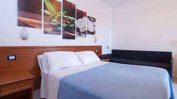 A hotel room with a large bed, a bedside table, a nightstand, a sofa, and three wall-mounted paintings.