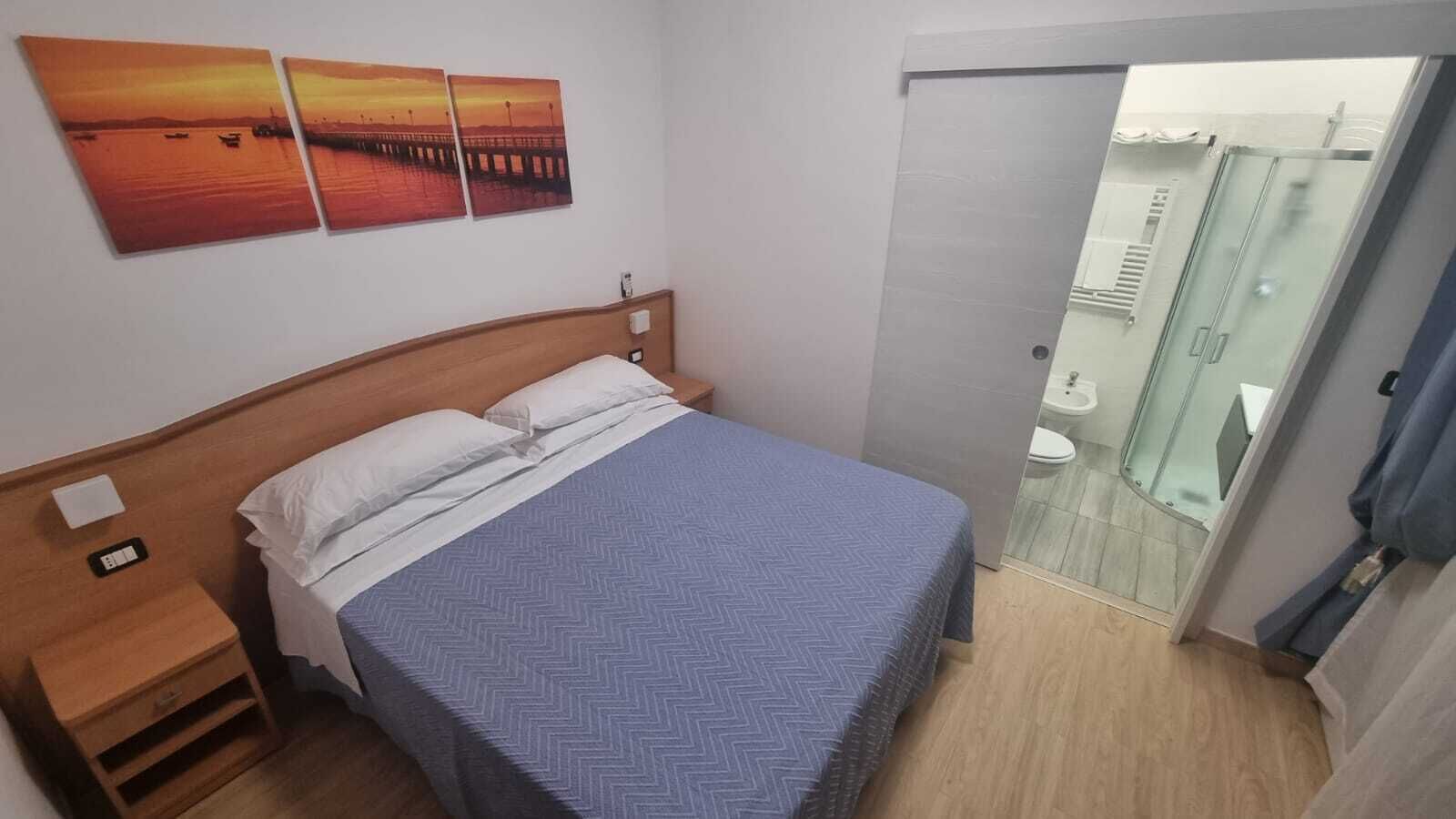 A hotel room with a bed, a nightstand, and a wall-mounted painting.