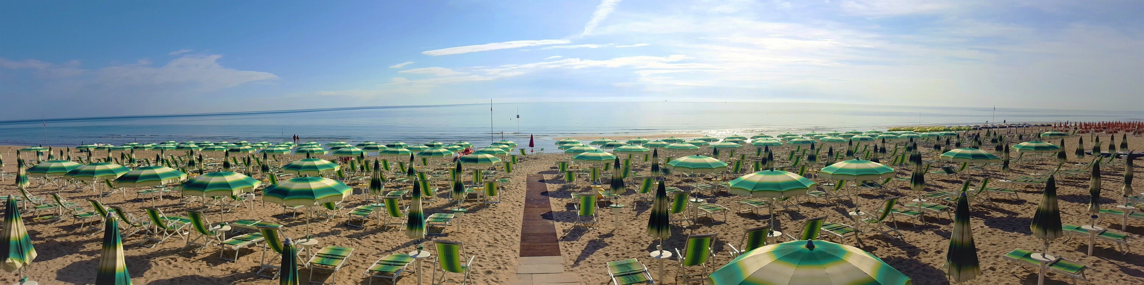 A beach with rows of green umbrellas and beach chairs, a clear sky, and a calm sea.