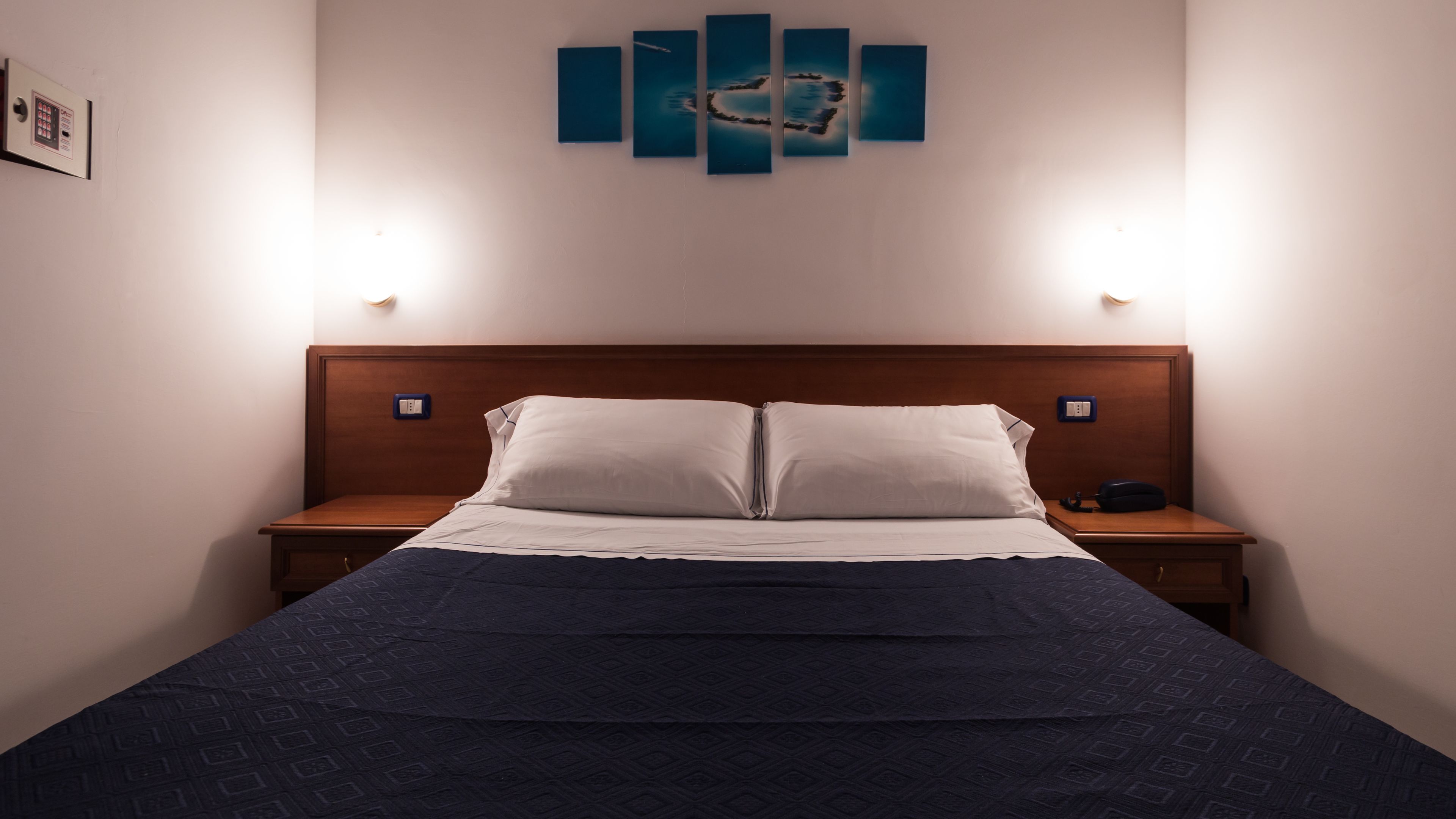 Un letto rifatto con una coperta a motivi, due comodini con lampade e un'opera d'arte appesa al muro sopra il letto.