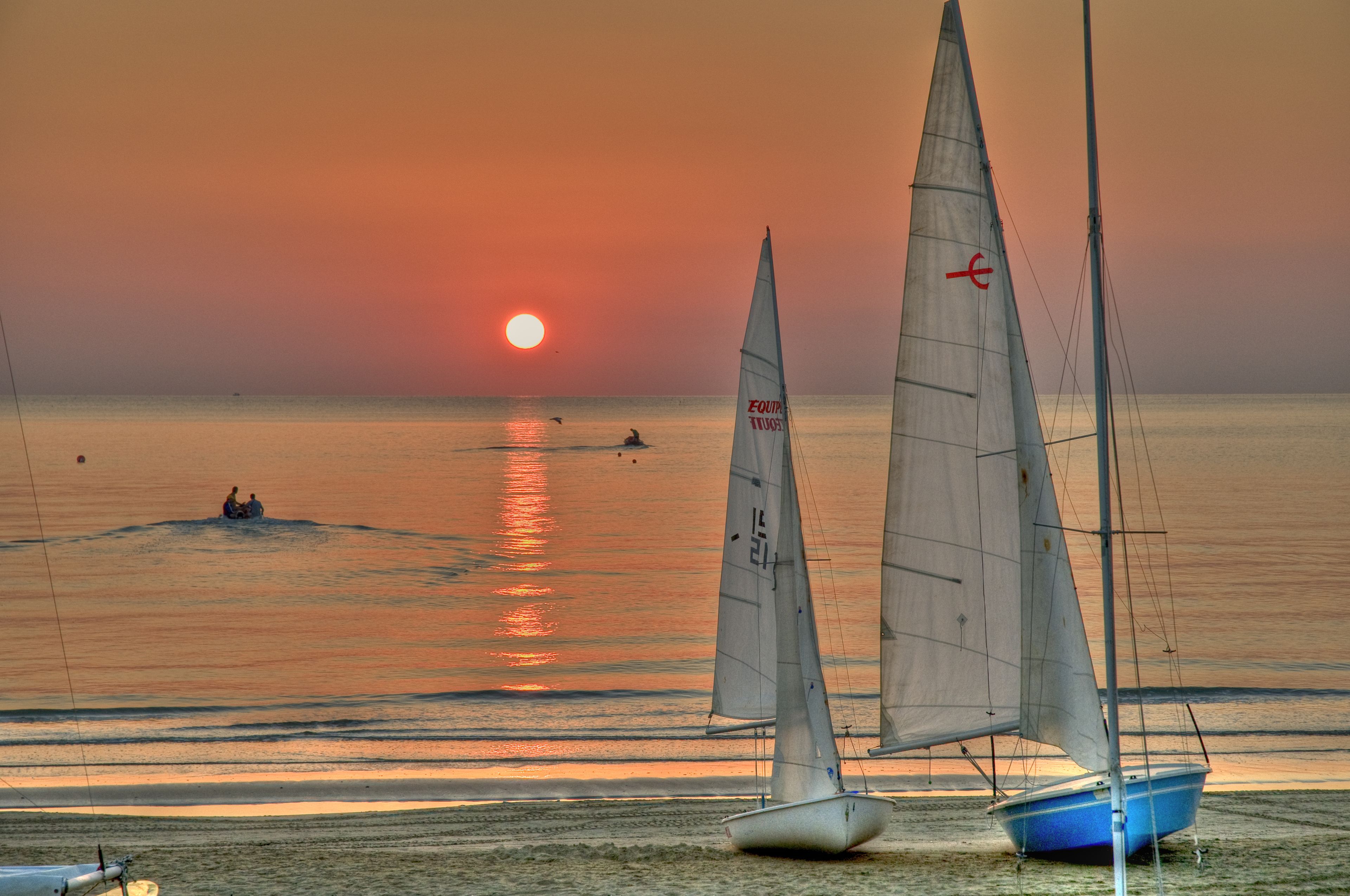 A beach scene with sailboats and a sunset.
