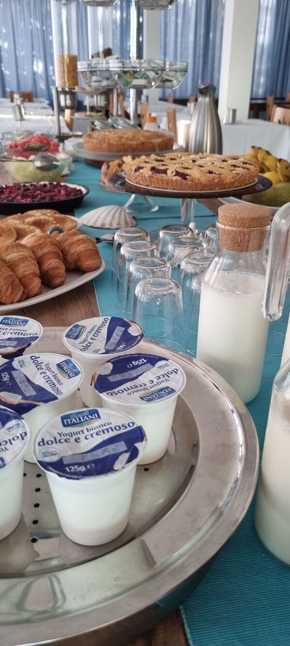 A buffet table with various food items including pastries, a cake, and bottles of milk. - Hotel Mare Blu (Pineto)