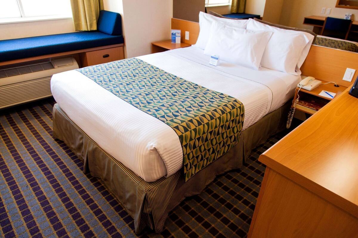 Een hotelkamer met een bed, nachtkastje, stoel en bureau met telefoon.