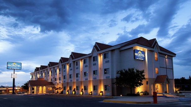 A Microtel by Wyndham hotel with a row of rooms, a parking lot, and a clear sky. - Microtel Inn & Suites by Wyndham Chihuahua (Chihuahua)