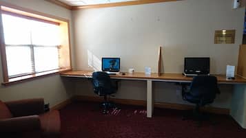 Une chambre d’hôtel avec deux bureaux, deux chaises, une fenêtre avec des stores et un sol recouvert de moquette.